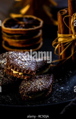 Foto verticale di diversi dolci marrone. I dolci sono farciti di crema, ricoperti da cioccolato e disseminata da bianco di scaglie di cocco. Alcuni bastoncini di cannella e s Foto Stock