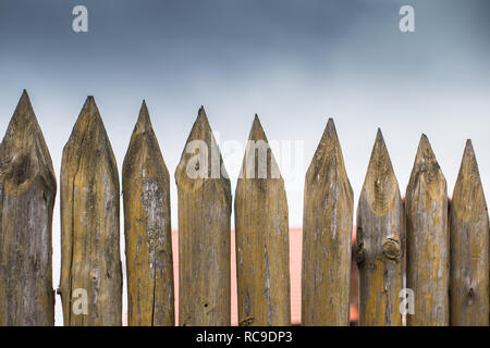 Recinzione fatta di sharp paletti di legno contro il cielo grigio. Foto Stock