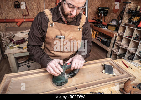 Falegname caucasica al lavoro utilizzando una smerigliatrice a nastro Foto Stock