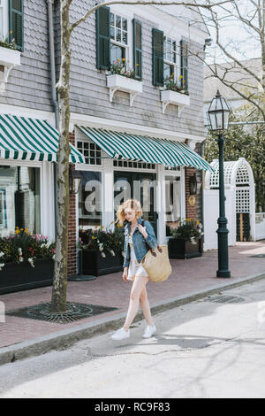 Giovane donna passeggiando lungo la strada che porta sacchetto di paglia, Menemsha, Martha's Vineyard, Massachusetts, STATI UNITI D'AMERICA Foto Stock