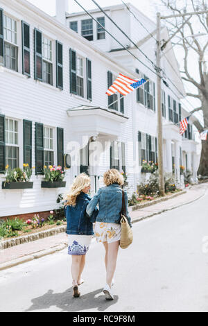 Due giovani amici di sesso femminile passeggiando lungo la strada del villaggio, vista posteriore, Menemsha, Martha's Vineyard, Massachusetts, STATI UNITI D'AMERICA Foto Stock