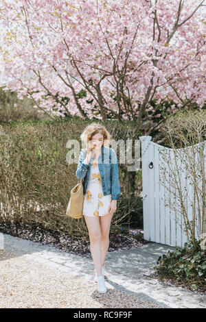 Giovane donna con borsa di paglia nella parte anteriore della struttura rosa blossom, Menemsha, Martha's Vineyard, Massachusetts, STATI UNITI D'AMERICA Foto Stock