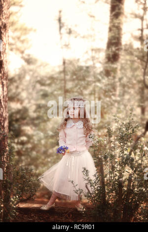 Bambina tutti abbigliati in piedi nei boschi che indossa una corona e tenendo i fiori nella sua mano. Foto Stock
