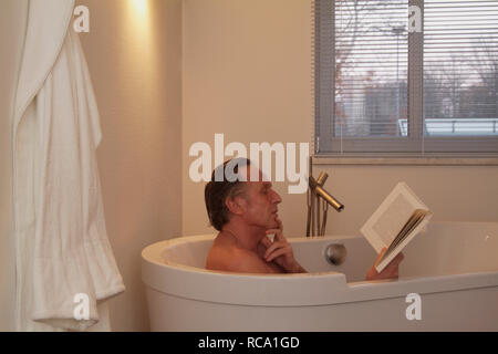 Mann mittleren altera liest ein Buch in der Badewanne | middleaged l uomo è la lettura di un libro in una vasca da bagno Foto Stock