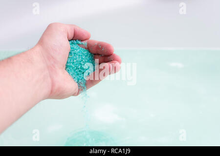 In prossimità dell'umana la mano bagno analizzato i cristalli di sale in acqua. Il trattamento termale, relax Foto Stock