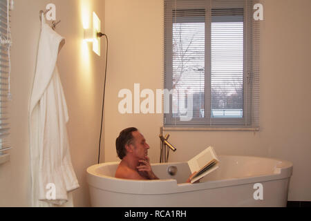 Mann mittleren altera liest ein Buch in der Badewanne | middleaged l uomo è la lettura di un libro in una vasca da bagno Foto Stock