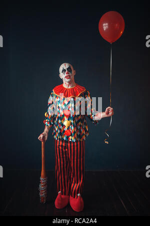 Brutto sanguinosa clown con la mazza da baseball e pallone aerostatico, horror. L'uomo con il trucco in costume di carnevale, crazy maniac Foto Stock