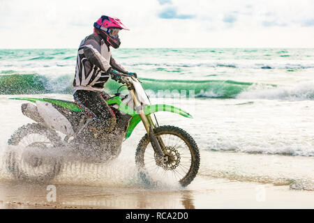 Motociclista in una tuta protettiva cavalca un motociclo sul mare, schizzi volare da sotto le ruote. Foto Stock