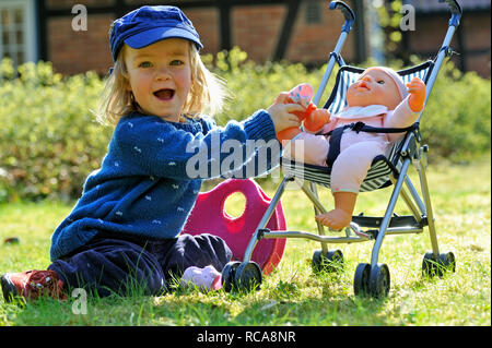 Kleines Mädchen, 2 Jahre alt, kümmert sich um ihre Puppe Puppenbuggy im | bambina di 2 anni, prendersi cura della sua bambola Foto Stock