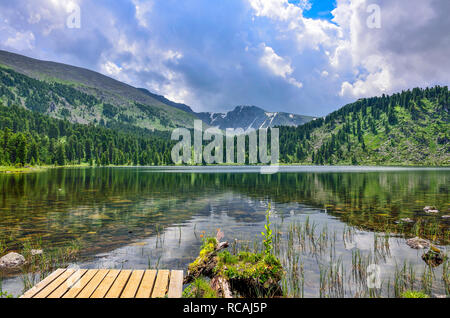 Uno da sette più pulito a Karakol montagna laghi con piattaforma di legno a sinistra, ai piedi dell'Bagatash pass, montagne di Altai, Russia. Per di conifere Foto Stock