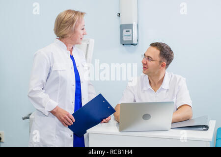 Medico e infermiere riesaminando le informazioni del paziente su un computer portatile in un ufficio Foto Stock