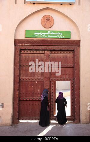 Donne velate a piedi attraverso una porta, di scena nel centro storico della città di Nizwa, Oman, Penisola Arabica, Medio Oriente e Asia Foto Stock