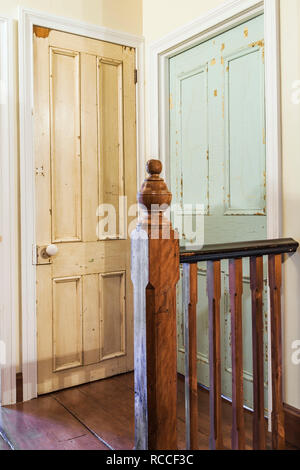 In legno post newel e ringhiera accanto al vecchio sbiadito vernice bianco armadio e camera da letto blu porte sul pavimento del piano superiore corridoio all'interno di vecchi 1835 fieldstone house Foto Stock