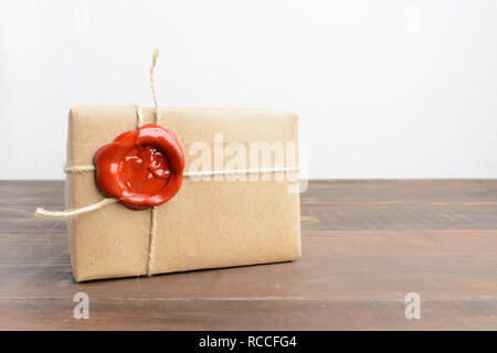 Uno presente nella carta craft con guarnizione rossa cera sopra un tavolo di legno e sfondo wite Foto Stock