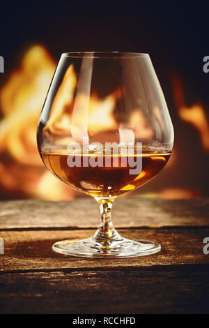 Il Brandy snifter con il cognac francesi su un vecchio rustico bancone bar davanti ad un fuoco ardente Foto Stock