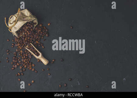 Il borsellino con fagioli arrosto e scoop di legno sulla pietra nera di calcestruzzo superficie testurizzata sfondo. Vista da sopra con copia spazio per il tuo testo. Foto Stock