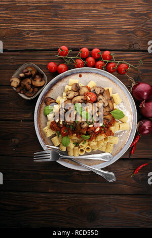 Penne pasta rigatoni in salsa di pomodoro con funghi, pomodori decorate con prezzemolo e basilico Foto Stock