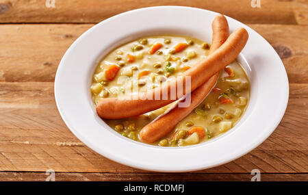 Verdure miste e la zuppa di piselli con bockwurst salsicce tedesche servite in una generica tazza bianca su legno Foto Stock