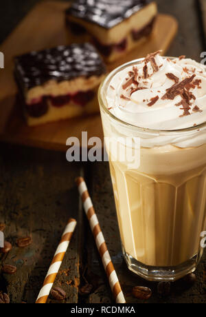 Il Cappuccino in vetro di elevata con topping di cioccolato servito con torta al cioccolato e caramelle on dark vecchio tavolo in legno. Visto da vicino da un angolo alto Foto Stock