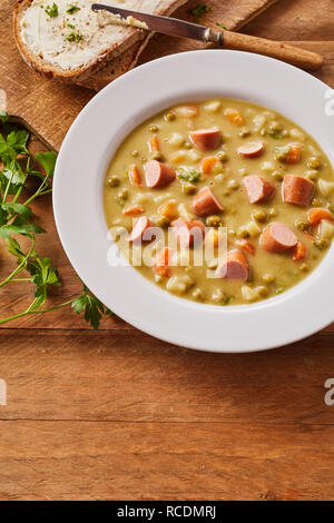 Ciotola di sana zuppa di piselli con cubetti di salsiccia bockwurst servita con pane su una tavola in legno rustico con spazio di copia Foto Stock