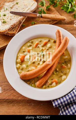 Bockwurst salsicce su una ciotola di zuppa di piselli con verdure miste visto dal di sopra con il pane affettato e igienico Foto Stock