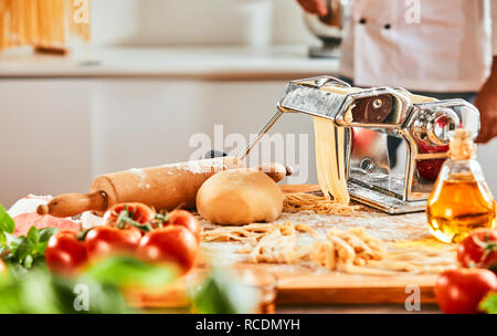 Lo Chef rendendo la pasta fatta in casa in una pizzeria pasta passando attraverso un coltello di metallo su un contatore con verdure fresche Foto Stock