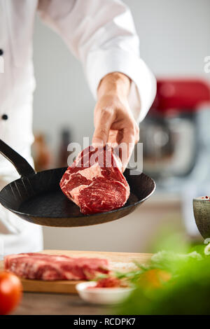 Lo Chef tenendo un materie in tenera età Scamone bistecca su una piccola vintage padella nera in una stretta fino alle mani Foto Stock