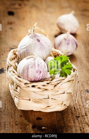 Piccolo appena raccolto le cipolle in un cesto tessuto con prezzemolo fresco su un rustico sfondo legno Foto Stock