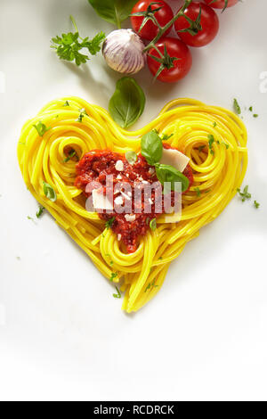 Decorazione a forma di cuore spaghetti bolognese conditi con salsa di pomodoro e formaggio parmigiano e basilico con ingredienti freschi sopra uno sfondo bianco Foto Stock