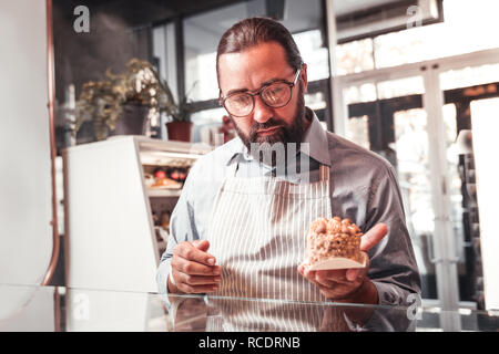 Uomo che indossa il grembiule tenendo una gustosa torta Foto Stock