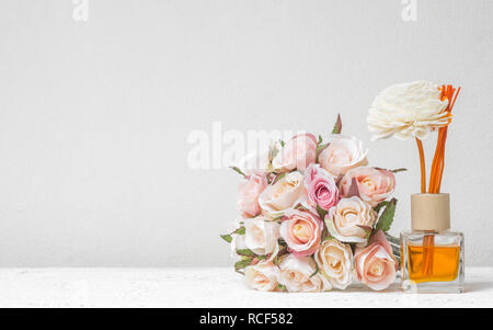 Reed aromatico rinfrescante, diffusore di fragranze Set di bottiglia con bastoni di aroma (reed diffusori) con rose fiore sul muro bianco sullo sfondo. Foto Stock