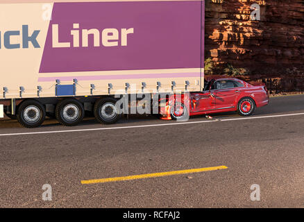 Due auto incidente. Si è schiantato vetture. Un rosso coupé/sedan contro il retro di un grosso camion. Grande danno. Sulla strada con sfondo dell'ambiente. Foto Stock