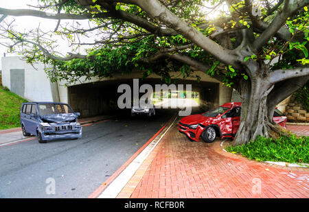 Due auto incidente. Si è schiantato vetture su strada in posizione. Una berlina rossa contro un albero dopo una collisione con un gret van. Foto Stock