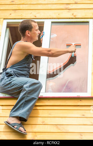 Maschio professionale in tuta pulisce la finestra della casa Foto Stock