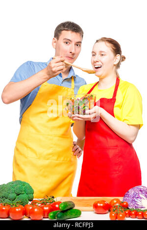 Un uomo con un cucchiaio di legno alimenta una ragazza con un utile insalata di verdure su sfondo bianco Foto Stock