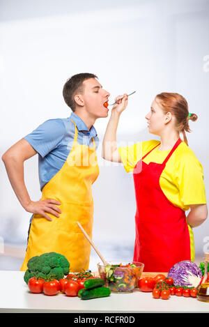 Una donna con un cucchiaio di legno alimenta un uomo una sana insalata di verdure in cucina Foto Stock