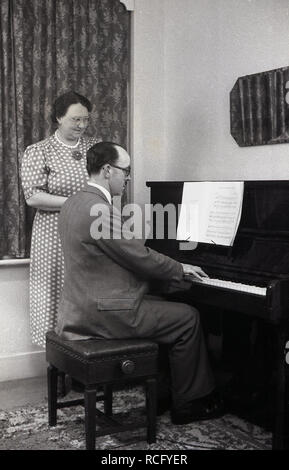 1950s, storico, a casa una moglie che guarda suo marito suonare il pianoforte, Inghilterra, Regno Unito. Nell'era precedente la televisione, l'intrattenimento domestico era fornito dalla radio, dai libri e dal suonare uno strumento musicale. Foto Stock