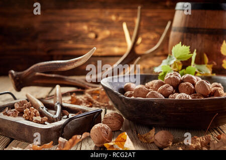 Pila di noci comuni in guscio e il dado cracker di close-up sul tavolo di legno in casa rustica con corna e il vecchio Barile di legno in background Foto Stock