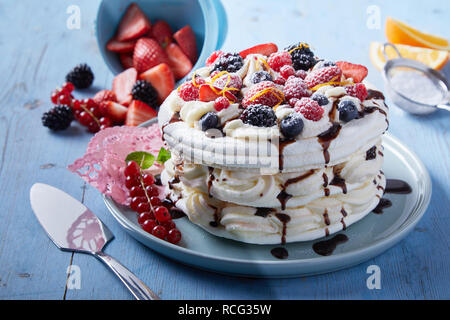 Deliziosa torta Pavlova con strati alternati di panna montata e meringa guarnita con frutti di bosco freschi e una spruzzata di sciroppo al cioccolato Foto Stock