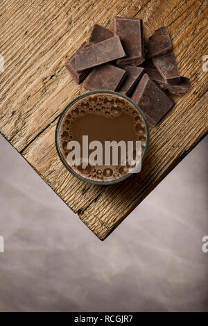 Bicchiere pieno di cioccolato al latte sul tavolo di legno con blocchi di cioccolato. Foto Stock