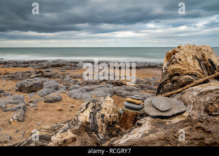 Una pila di pietra su un tronco di albero, sotto un cielo drammatico su una spiaggia sassosa, visto a Cocklawburn Beach vicino a Berwick-upon-Tweed in Northumberland, England, Regno Unito Foto Stock