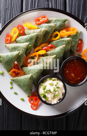 La cucina indiana spinaci samosa servita con verdure e due salse close-up su una piastra sul tavolo. Verticale in alto vista da sopra Foto Stock