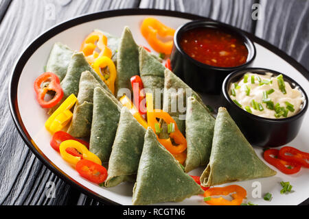 La cucina indiana spinaci samosa servita con verdure e due salse close-up su una piastra sul tavolo orizzontale. Foto Stock