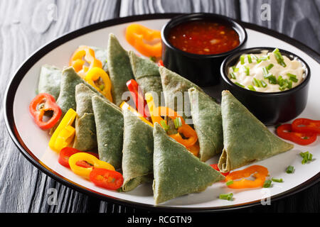 Gli spinaci samosa servita con verdure e due salse close-up su una piastra sul tavolo orizzontale. Foto Stock