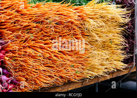 Orange baby carote e ravanelli impilati sul tavolo nel mercato locale Foto Stock