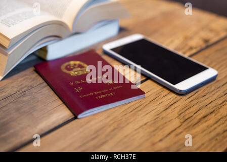 Passaporto cinese e lo smartphone su un tavolo di legno con un libro aperto in un coffee shop Foto Stock