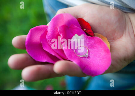 Un anello di diamante si trova in mano su petali di rose. Close up foto Foto Stock