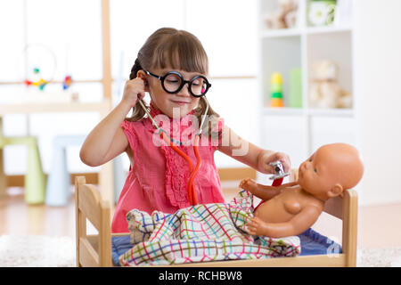 Ritratto di bambino felice una ragazza 3 anni con gli occhiali a casa o nursery room con bambola, riproduzione di medico Foto Stock