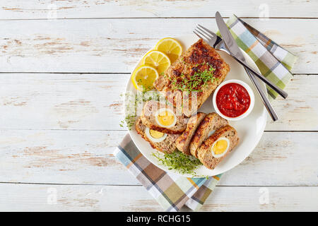 Vista aerea di fettine di polpettone servito con salsa di pomodoro e le fette di limone su una piastra bianca su un vecchio tavolo di legno, vista da sopra, close-up, flatla Foto Stock