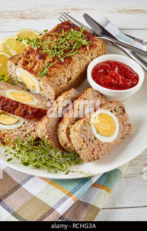 Fette di polpettone farcito con uova sode servite con salsa di pomodoro e le fette di limone su una piastra bianca su un vecchio tavolo di legno, vista verticale da ab Foto Stock